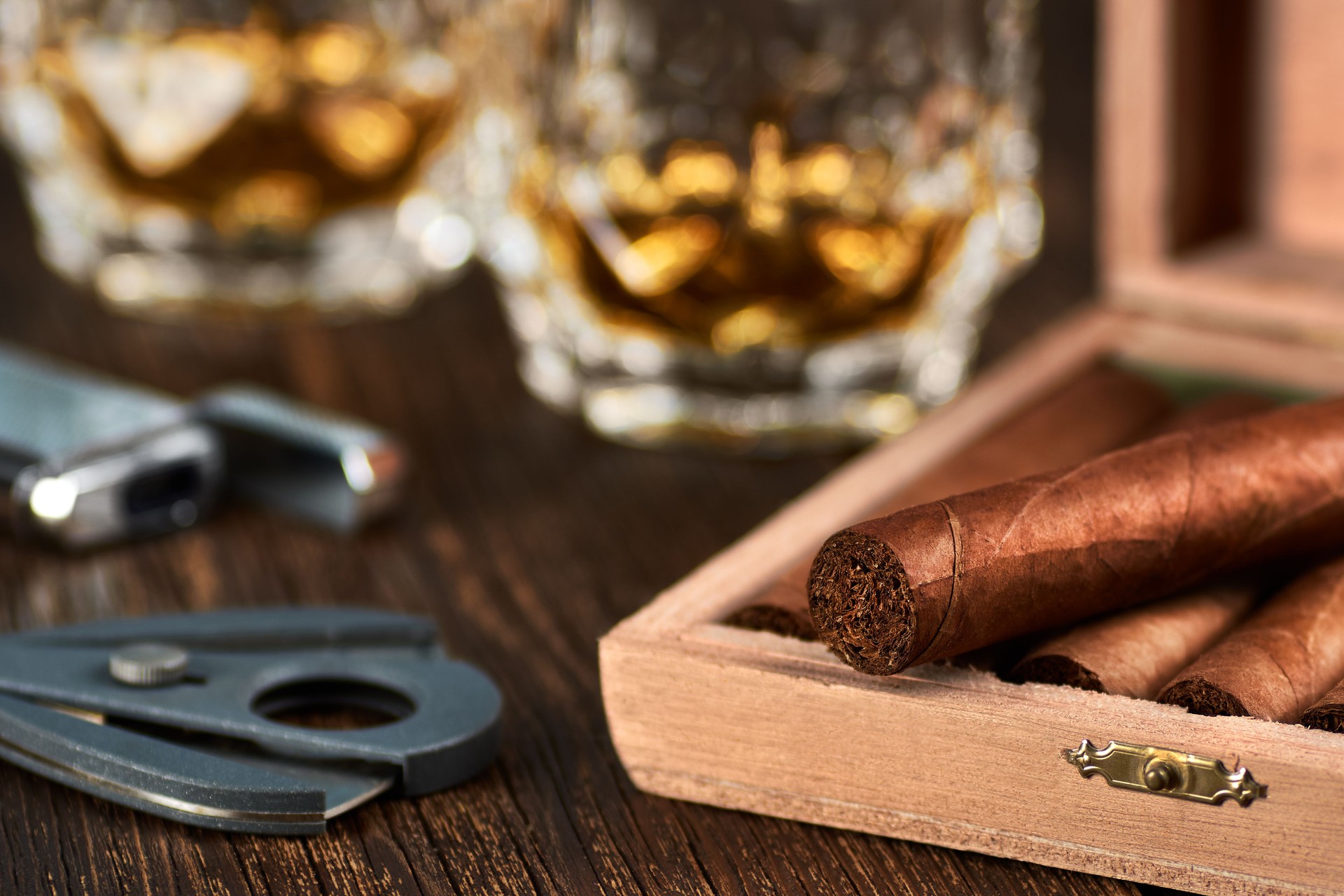 View of a wooden box with Cuban cigars, a lighter and a cutter. Still life with two glasses of whiskey on the table.